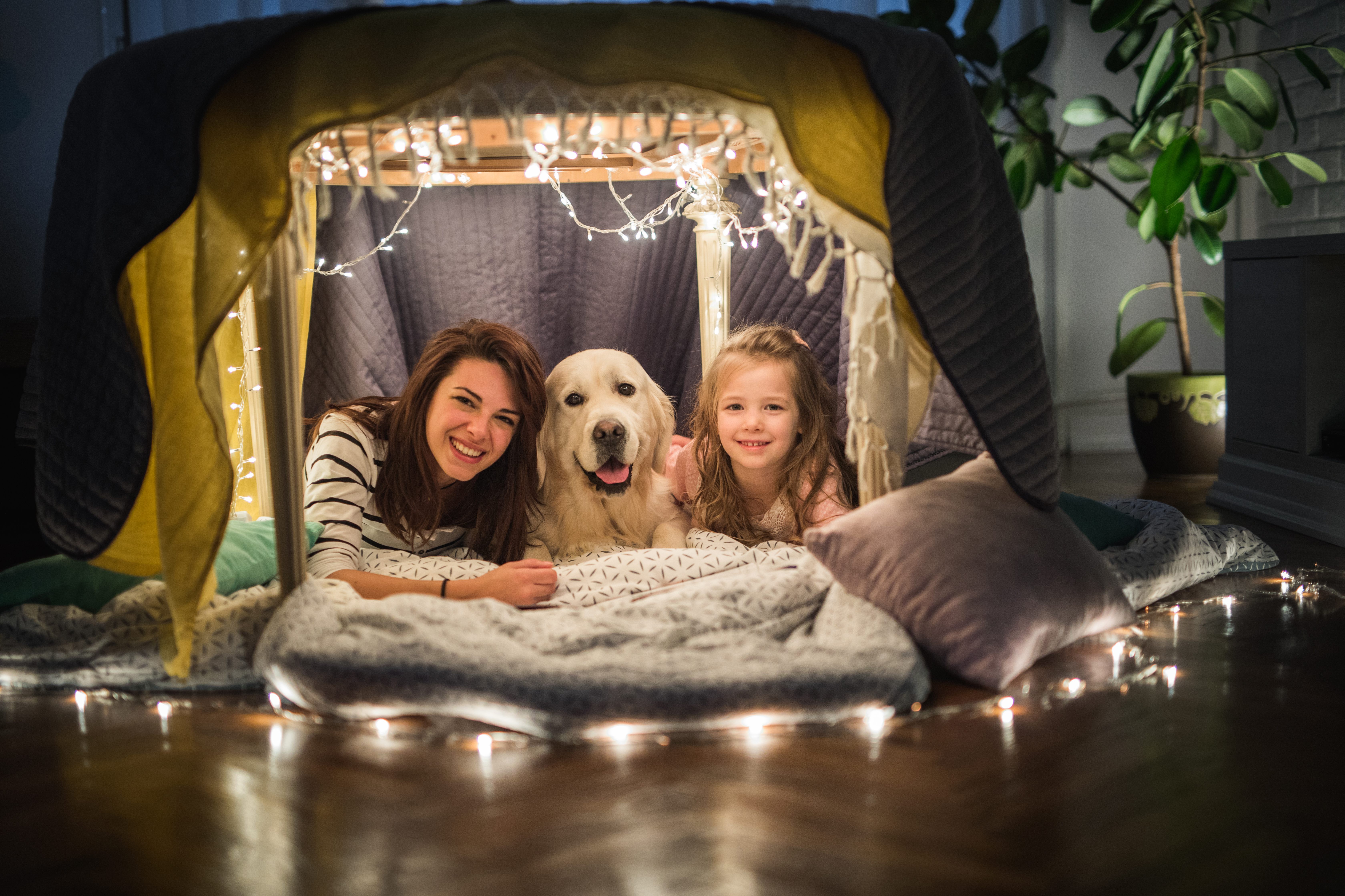 Happy mother and daughter relaxing with a dog in a tent at home.
